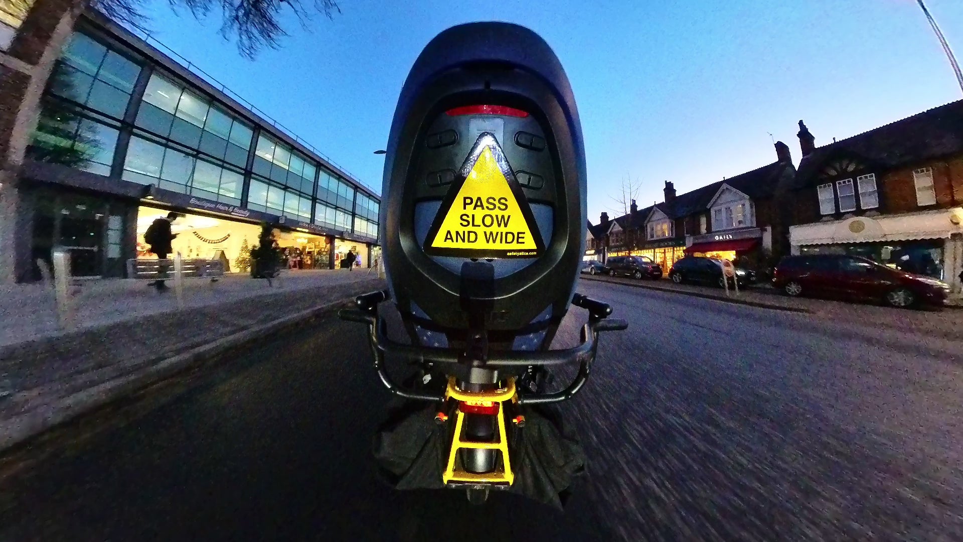 Load video: Bicycle with child seat travelling through traffic at night with a Pass Slow and Wide sticker on the back